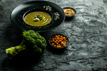 broccoli soup with the addition of pumpkin seeds, sesame on a black plate, next to crispy, soy-nut additions