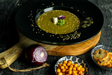 broccoli soup with the addition of pumpkin seeds, sesame on a black plate, next to crispy, soy-nut additions
