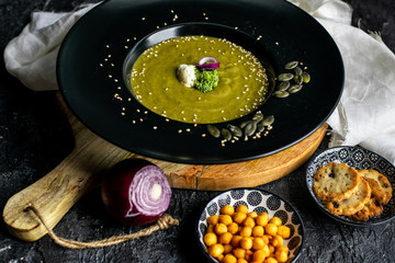 broccoli soup with the addition of pumpkin seeds, sesame on a black plate, next to crispy, soy-nut additions