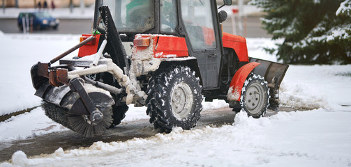 Red tractor clearing snow on footpath, with snow plow and rotating brush. Municipal service...
