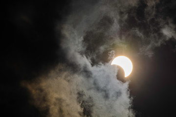 a partially eclipsed sun behind wispy clouds. The sun is a bright, white circle with a dark...
