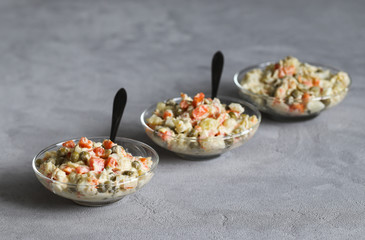 Russian salad with chicken, potatoes, eggs, carrots, green peas and cucumber, appetizer on a light gray background