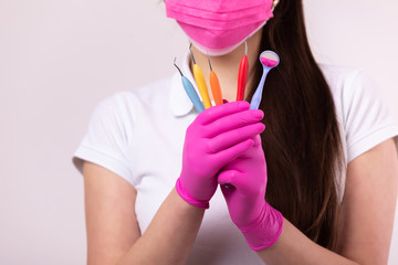 people, medicine, dentistry and healthcare concept - dentist woman in pink face mask and medical gloves with colored tools on white background. dentist for children