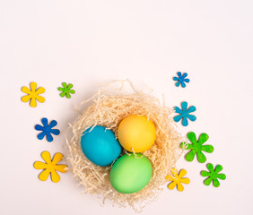 yellow, green and blue egg in the nest, light background, bright card, Easter greetings, top view, place for text