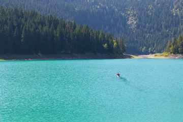 A small boat with people in the middle of a beautiful lake. On the background of picturesque nature.