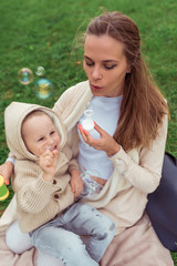 Mom woman plays with child, little boy son, autumn on street, blowing soap bubbles, balloons, warm casual clothes, grass lawn background. Emotions of love caring relaxing weekend.