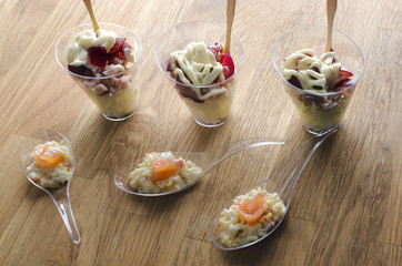 Event catering: Disposable plastic cups with snacks - salad with ham, sauce, salmon and grapes, close up