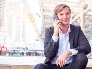 Portrait of young businessman sitting and talking on mobile phone with smiling at the city.