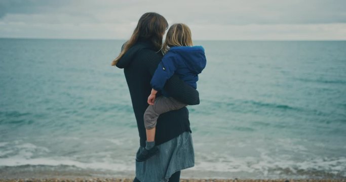 Young mother standing by the sea with toddler in her arms