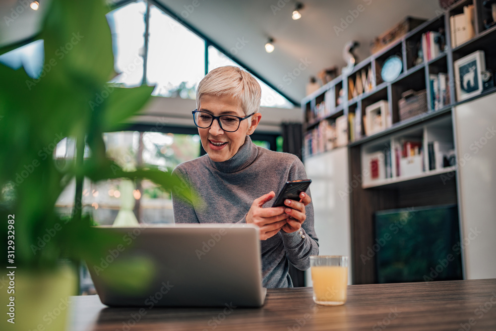 Wall mural modern senior woman using smart phone and laptop, portrait.