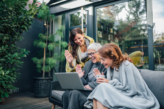 Family of three beautiful women having video call on laptop in the home garden.