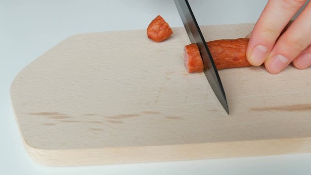 Female hands cut slice hunting sausage on a wooden kitchen board with a black ceramic knife