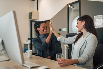 Two excited businesswoman high five in modern office.