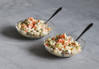 Russian salad with chicken, potatoes, eggs, carrots, green peas and cucumber, appetizer on a light gray background