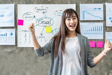 Portrait of Happy asian woman standing and cheerful in office workplace with document plan and goal on wall background. Headshot of smiling employee team leader leaning table with feeling confident