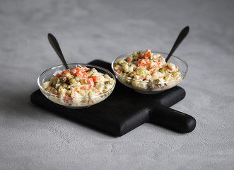 Russian salad with chicken, potatoes, eggs, carrots, green peas and cucumber, appetizer on a light gray background