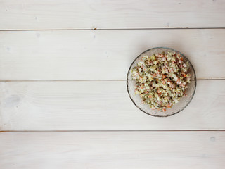 Traditional russian salad from boiled vegetables and sausage with sauce in bowl. Russian New Year or Christmas salad on light background. Top view, flat lay