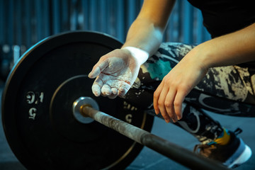 Caucasian teenage girl practicing in weightlifting in gym. Female sportive model preapring for training with barbell, looks concentrated. Body building, healthy lifestyle, movement and action concept.
