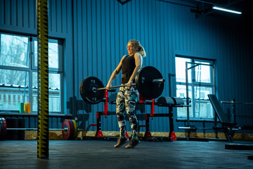 Obraz na płótnie Canvas Caucasian teenage girl practicing in weightlifting in gym. Female sportive model training with barbell, looks concentrated and confident. Body building, healthy lifestyle, movement and action concept.