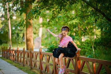 Naklejka premium Beautiful little cheerful girl with long well-groomed hair in a fluffy tutu skirt jumps from a high wooden fence