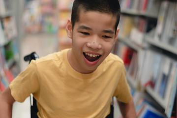Disabled child on wheelchair having fun choosing books from shelves, Special children's lifestyle, Life in the education age of special need kids, Happy disability kid concept, Selective focus.