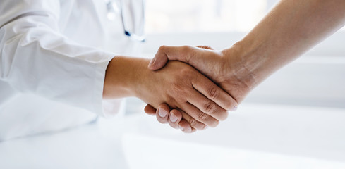 Female doctor shaking hands with man in medical office