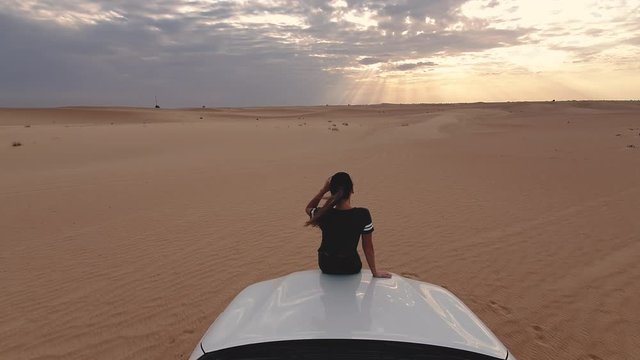 Young traveller woman sitting on the car in desert. Travel concept.