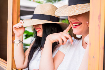 Close up portrait of young caucasian couple of girls smile and laugh hidden by fashioon hats -...