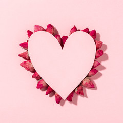 Conceptual background of Valentine's day, pink heart made of paper on white background, dry rose flowers arranged on the contour of the heart shape.