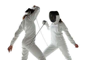 Teen girls in fencing costumes with swords in hands isolated on white studio background. Young...