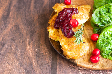 Traditional Viennese chicken schnitzel served with cranberry sauce and green salad. Wooden background. Chicken steak in breading, sauce and fresh salad. 