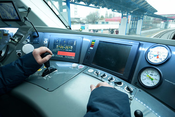 Train driver’s hand touching the start lever on the dashboard. At the cabin of the passenger train. 