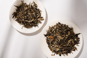 Dry green tea leaves on a white plate, the shadow of trees on the background