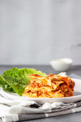 Portion of traditional Italian lasagna with minced meat, tomato and cheese served with green salad on a plate. Light grey concrete background, selective focus.