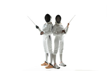 Teen girls in fencing costumes with swords in hands isolated on white studio background. Young...