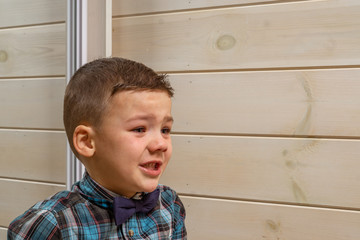 A 4 years old boy in a blue clerical shirt is crying on a light wooden background.