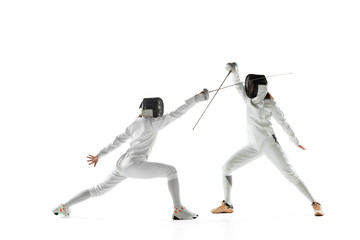 Teen girls in fencing costumes with swords in hands isolated on white studio background. Young...