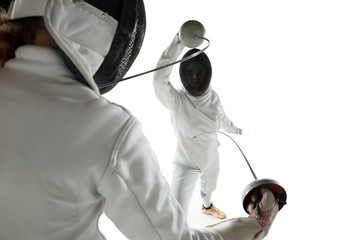 Teen girls in fencing costumes with swords in hands isolated on white studio background. Young...