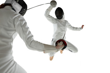 Teen girls in fencing costumes with swords in hands isolated on white studio background. Young...