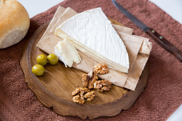 horizontal photo, brie cheese with nuts and olives lies on a wooden board near freshly rolled buns and a knife