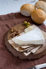 vertical photo, brie cheese next to lie nuts and olives on a wooden board next to fresh buns