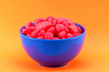 Rote Fruchtgummis in blauer Keramikschale isoliert auf orangefarbenen Hintergrund
