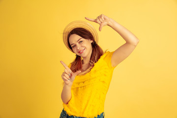 Framing, selfie, smiling. Caucasian woman's portrait on yellow studio background. Beautiful female model in hat. Concept of human emotions, facial expression, sales, ad. Summertime, travel, resort.