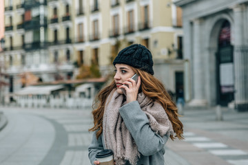 Fototapeta premium Caucasian blonde girl looks to the left side while talking with her mobile phone in the middle of a European city