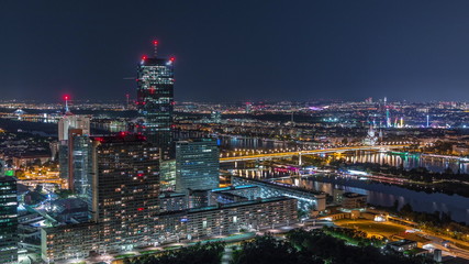 Obraz premium Aerial panoramic view over Vienna city with skyscrapers, historic buildings and a riverside promenade night timelapse in Austria.