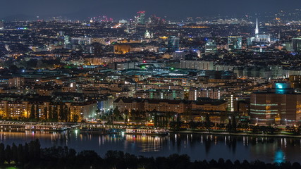 Obraz premium Aerial panoramic view over Vienna city with skyscrapers, historic buildings and a riverside promenade night timelapse in Austria.