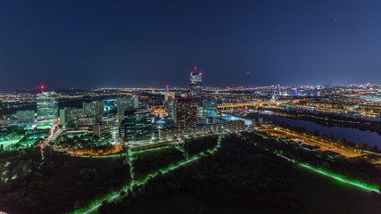 Aerial panoramic view over Vienna city with skyscrapers, historic buildings and a riverside promenade night timelapse in Austria.