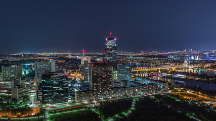Aerial panoramic view over Vienna city with skyscrapers, historic buildings and a riverside promenade night timelapse in Austria.