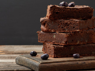 stack of square baked slices of brownie chocolate cake with walnuts on a wooden surface. Cooked homemade food