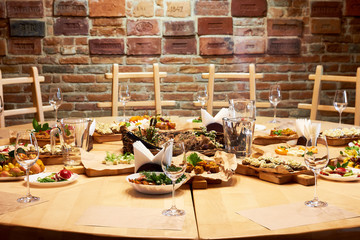 Wooden table with a set of variety snacks, different vegetable salads, salad, pickle carrot, kavarma, rye bread sandwiches with soft cheese cream against a brick wall